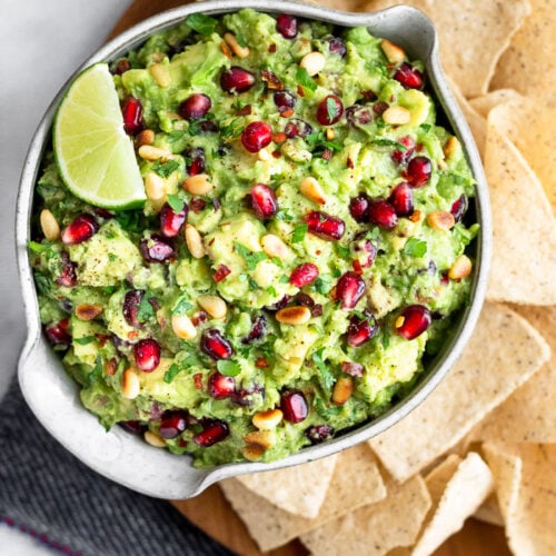 Large plate filled with chips and a bowl of pomegranate guacamole topped with a lime wedge.