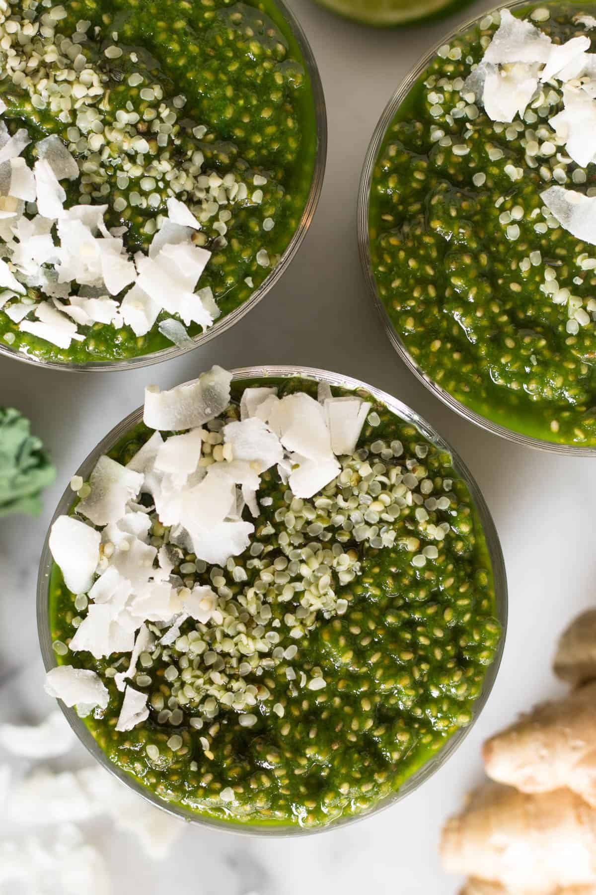 Overhead shot of 3 glasses with green juice chia pudding and toppings in them
