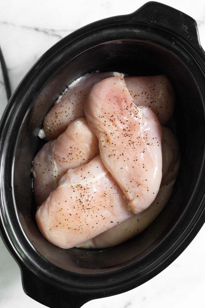 Crockpot filled with raw chicken sprinkled with salt and pepper.