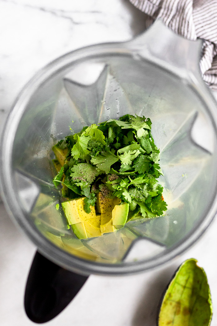 Blender filled with avocado, cilantro, and salt and pepper.