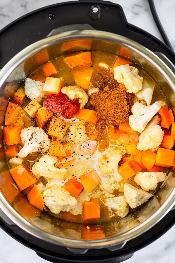Instant Pot filled with cubed butternut squash, cauliflower florets, broth, coconut milk, spices, curry paste, and salt and pepper.