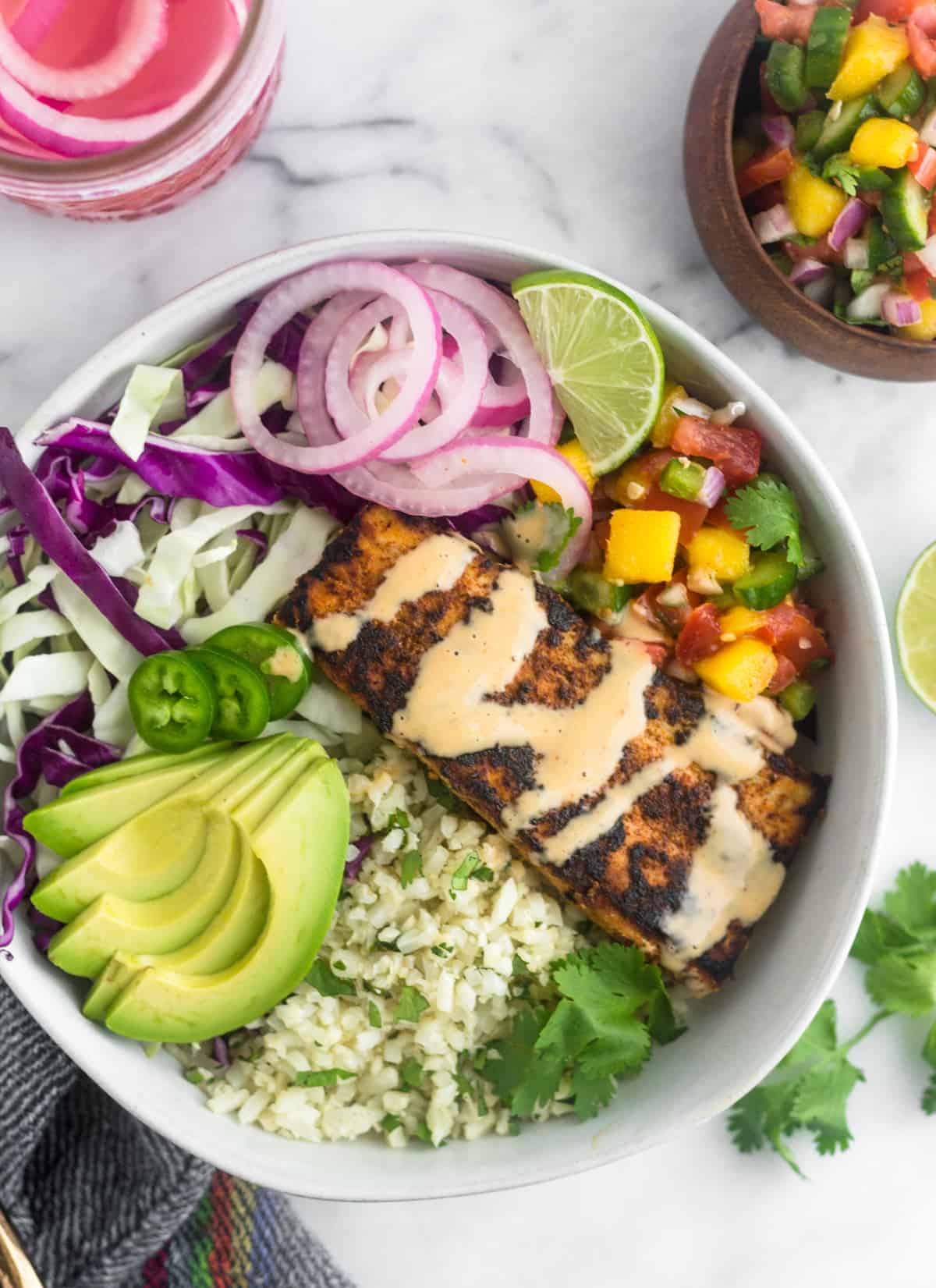 A Whole30 fish taco bowl loaded with cauliflower rice, shredded cabbage, blackened fish, mango salsa, pickled onions, and avocado