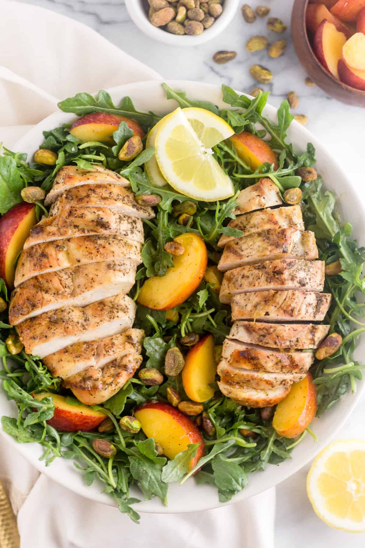 Large white bowl filled with a Peach and Pistachio Salad with Grilled Chicken on top of a white linen