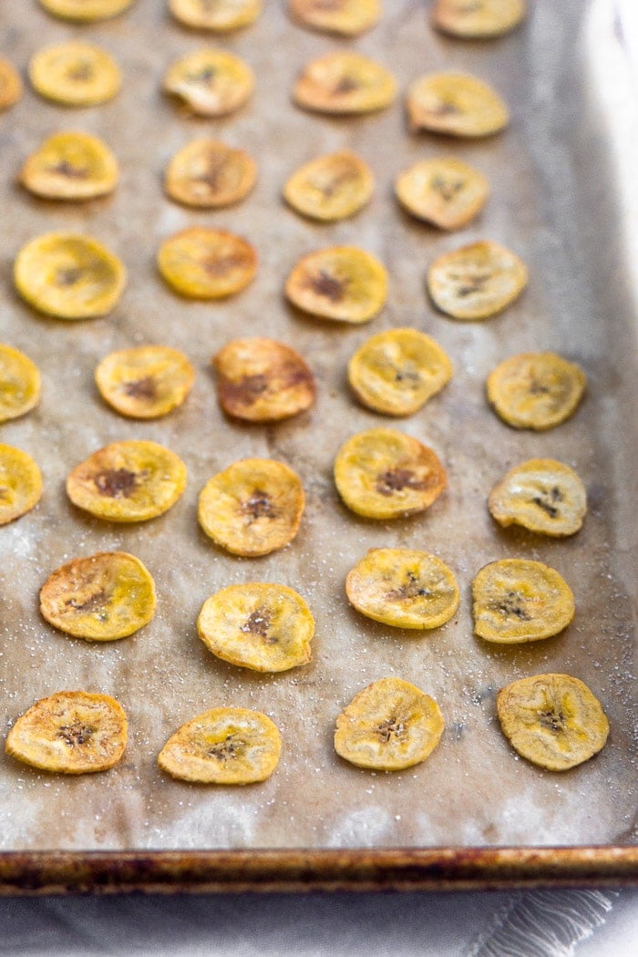 Baked plantain chips spread out on a baking sheet.