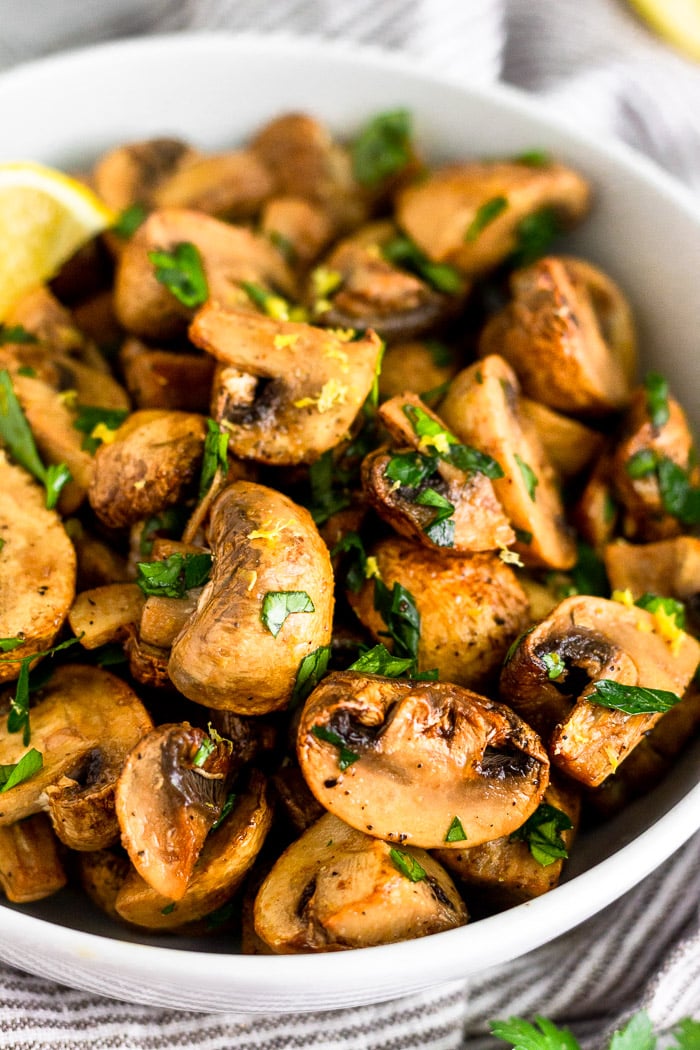 Close up of a bowl filled with oven roasted mushrooms topped with fresh parsley and lemon zest.