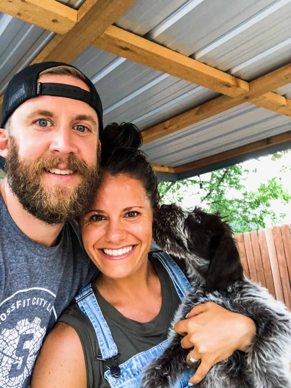 Man and woman taking selfie holding a new puppy that is licking the girl's face