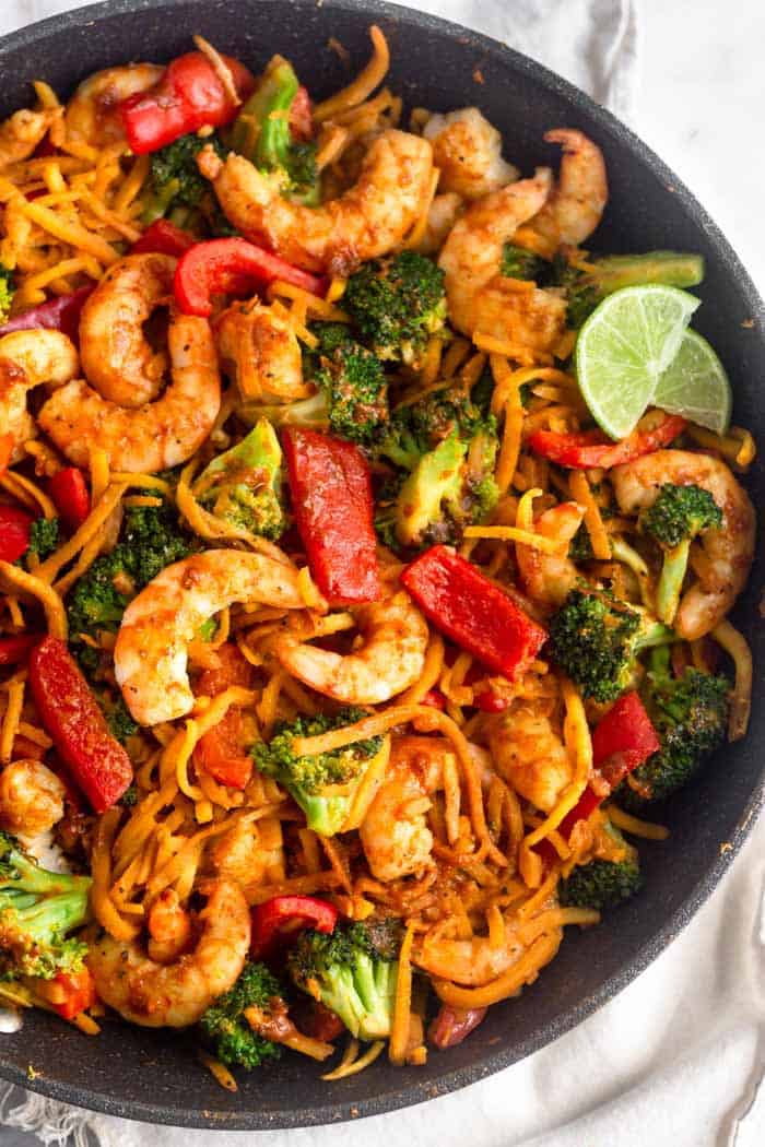 Large pan of paleo and Whole30 Shrimp & Butternut Squash Noodles with Curry Peanut Sauce with two lime wedges as a garnish.