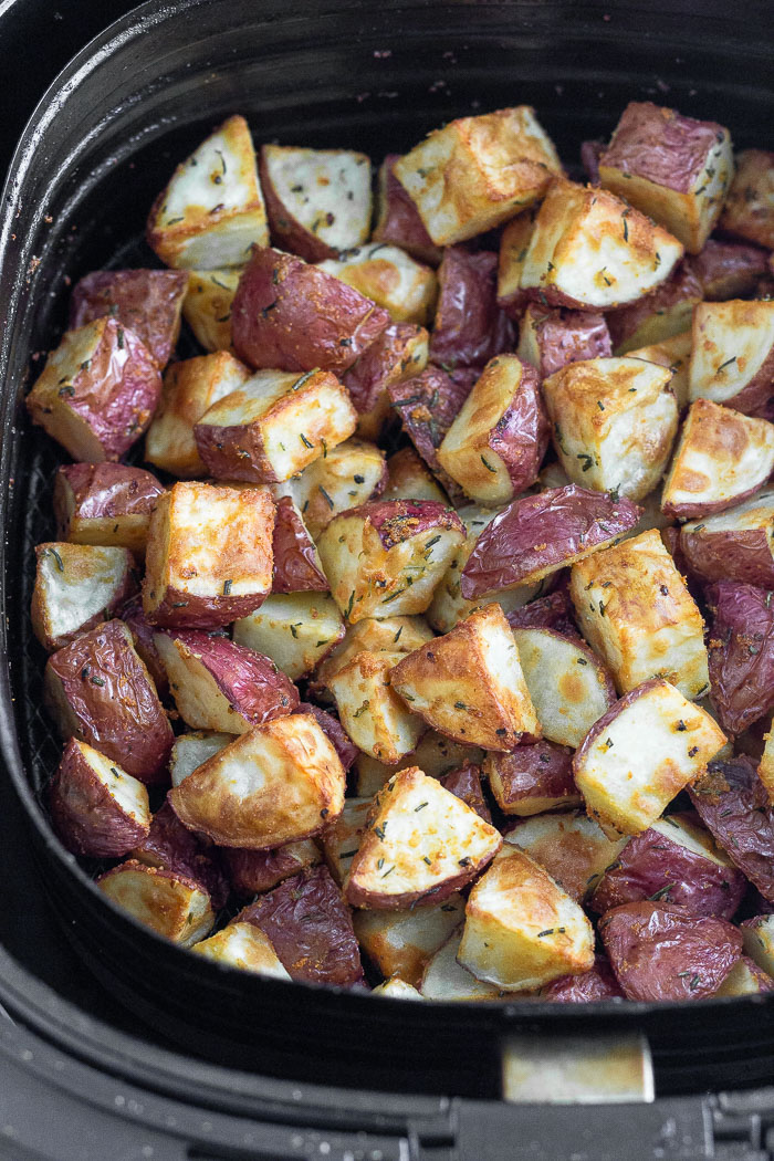 Crispy rosemary potatoes in an air fryer basket that have just been cooked.