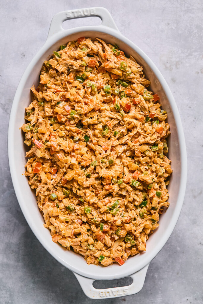 A mixture of shredded chicken and veggies in a creamy red sauce in a white au gratin dish before it is baked.