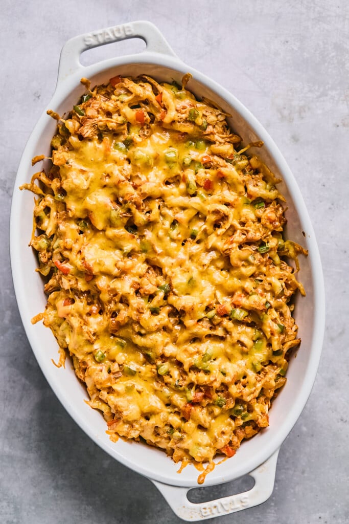 Chicken and veggies dip topped with melted cheese in a white au gratin dish.