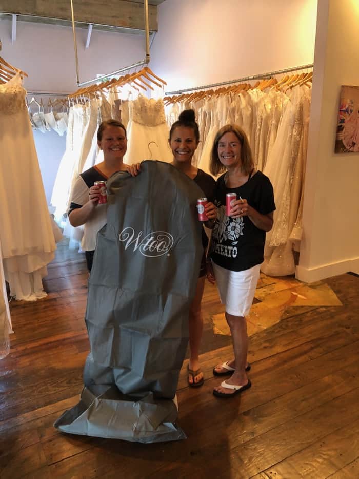 Girl with her mom and her sister holding her wedding dress in a large garment bag.
