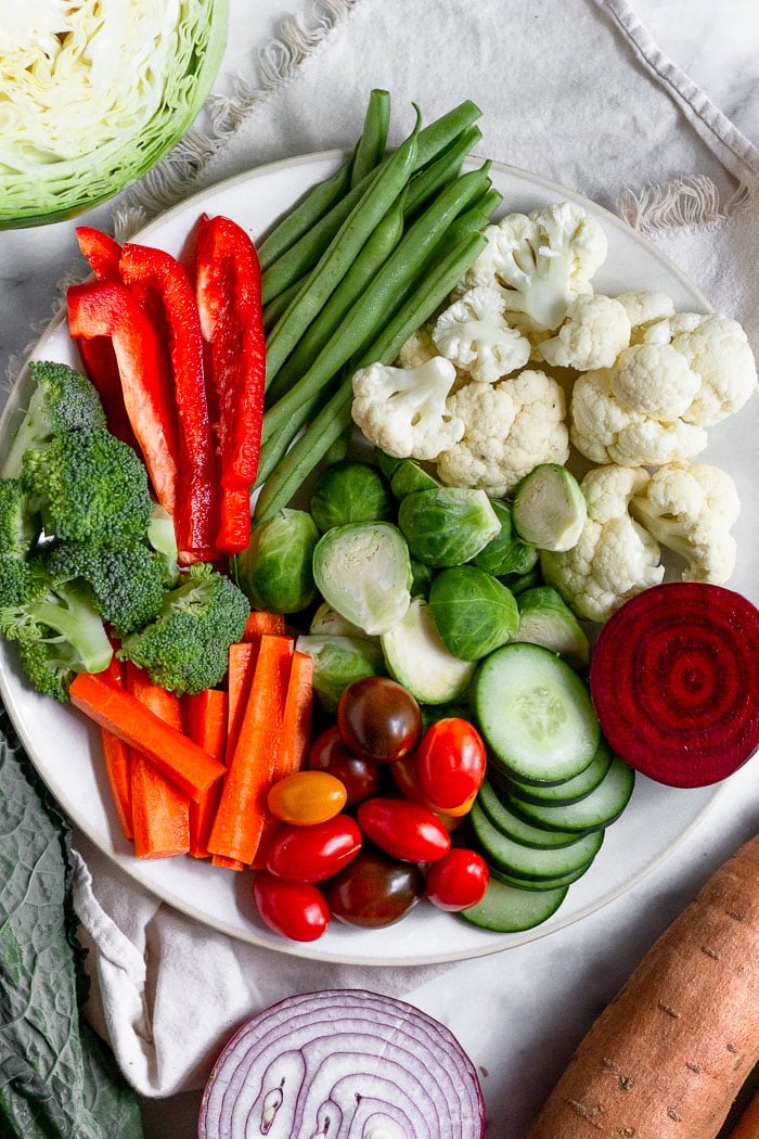 Large plate filled with multiple kinds of veggies cut up. Surrounded it is sweet potatoes, half a red onion, kale, and half a head of cabbage. Lots of veggies are shown for ETGveggies, a 5-day veggie challenge.