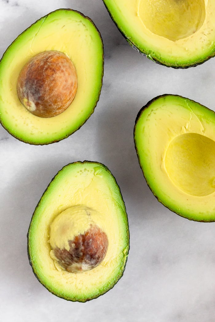 Four avocado halves on a white marble counter top.
