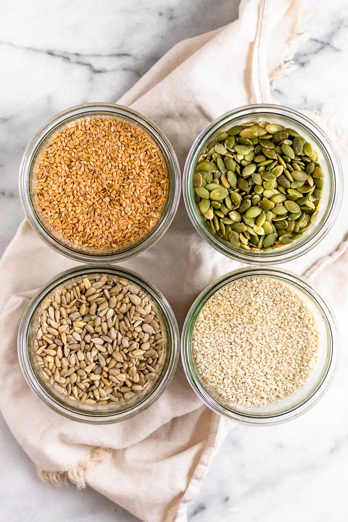 4 large jars filled with different seeds - flax, pumpkin, sesame, and sunflower - all for seed cycling.