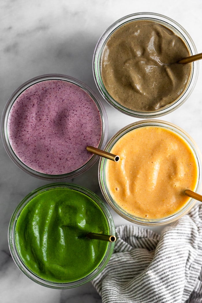 Four jars filled with four different smoothie flavors. Each one has a straw in it.