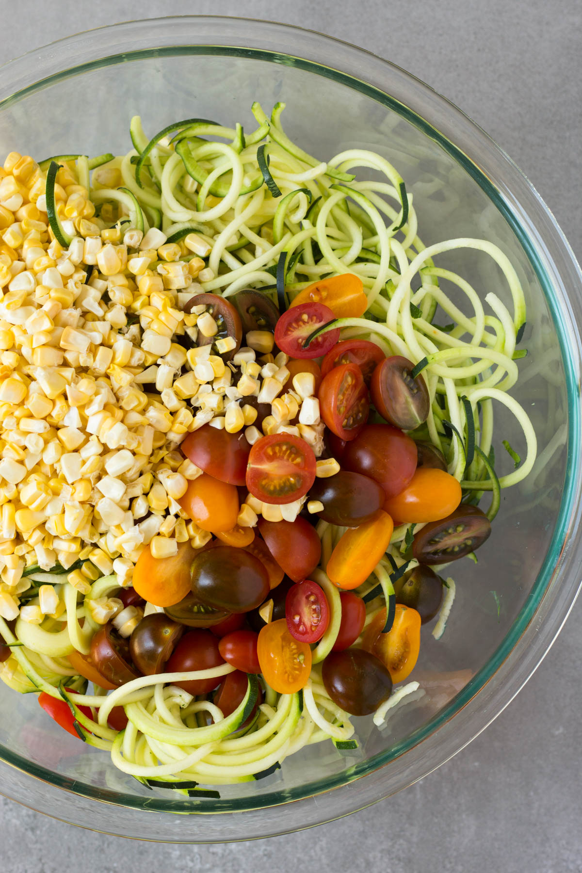 Large glass bowl filled with zucchini noodles, corn, and halved cherry tomatoes.