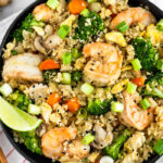 Large bowl of paleo cauliflower shrimp fried rice garnished with green onions and a lime wedge. The bowl is sitting on a stripped towel with chopsticks, ginger, a lime wedge, and green onions around it.
