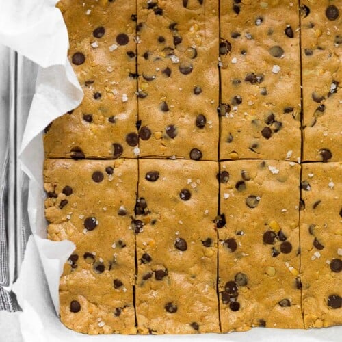 Glass pan lined with parchment paper filled with chocolate chip peanut butter perfect bar recipe.