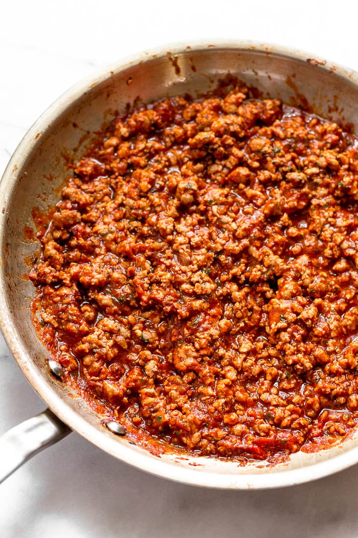 A large saute pan filled with sautéed ground pork, pizza sauce, and spices,