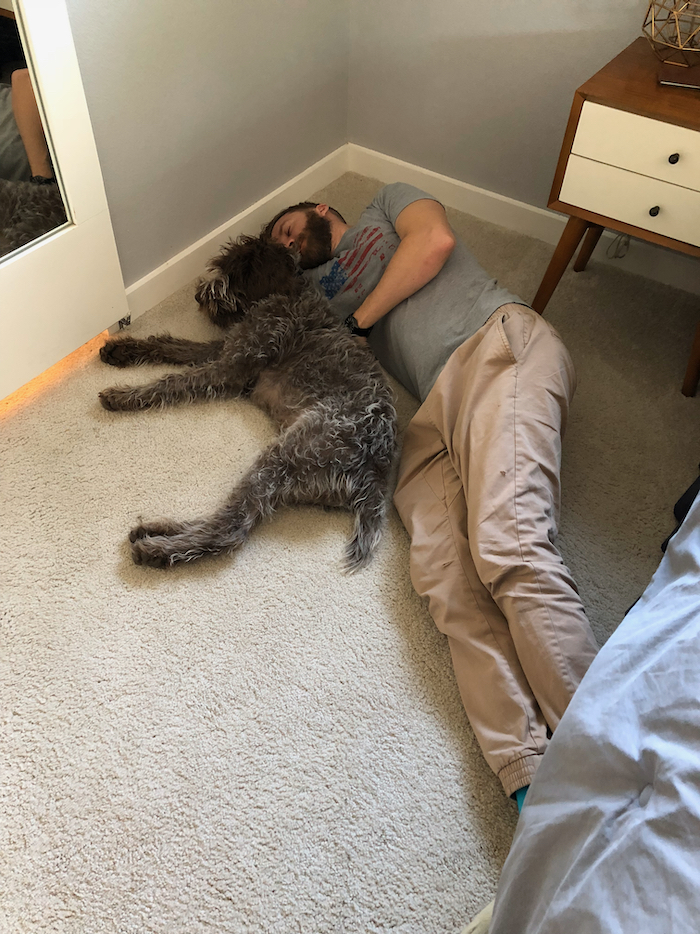 A man and a puppy laying on the ground snuggling.