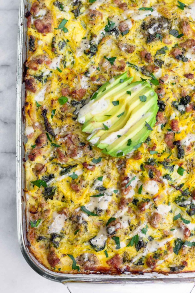 Overhead shot of spaghetti squash ground turkey casserole in a large baking dish. It is topped with sliced avocado, ranch dressing, and parsley.
