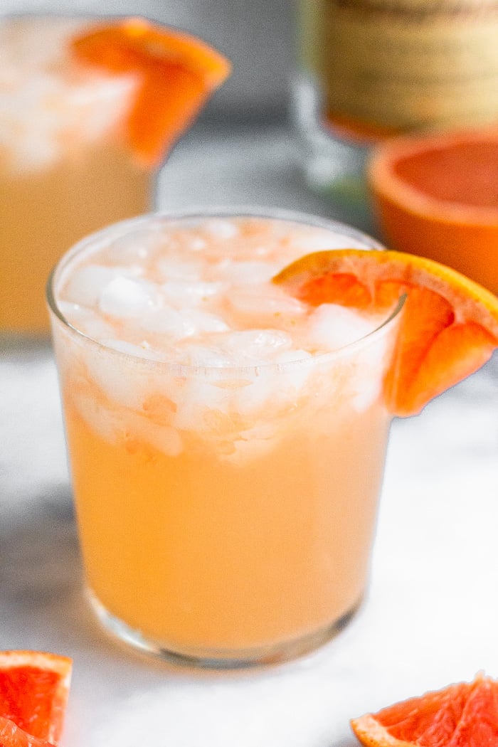 Close up of a grapefruit crush with a grapefruit wedge in it. Behind it is another one and half a grapefruit.