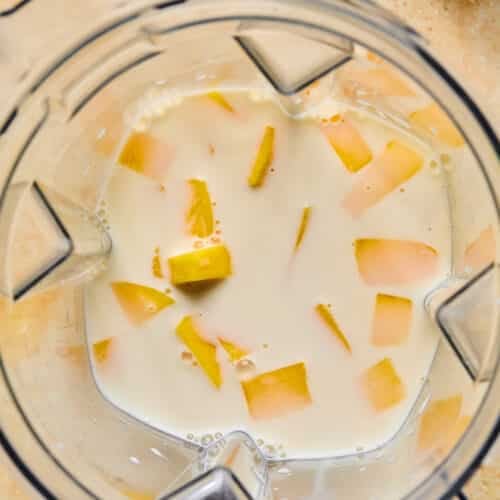 Overhead shot of a blender with milk and diced mangos in it.