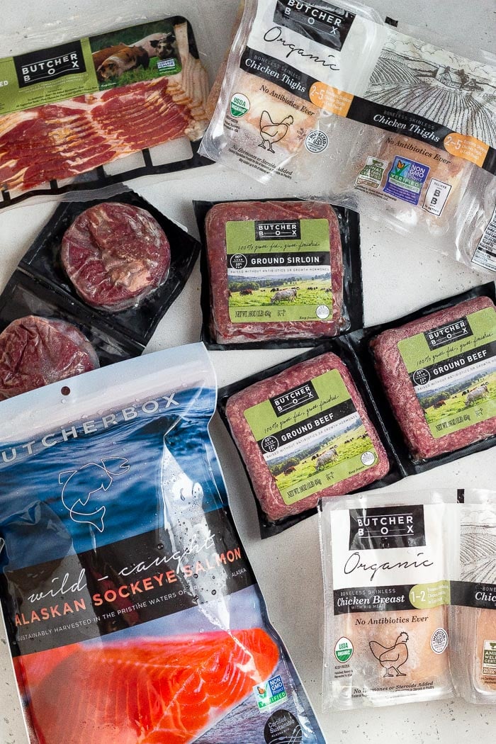 An overhead shot of a bunch of meat from ButcherBox - a pack of bacon, chicken breakfast, ground beef, chicken thighs, salmon, and steak.