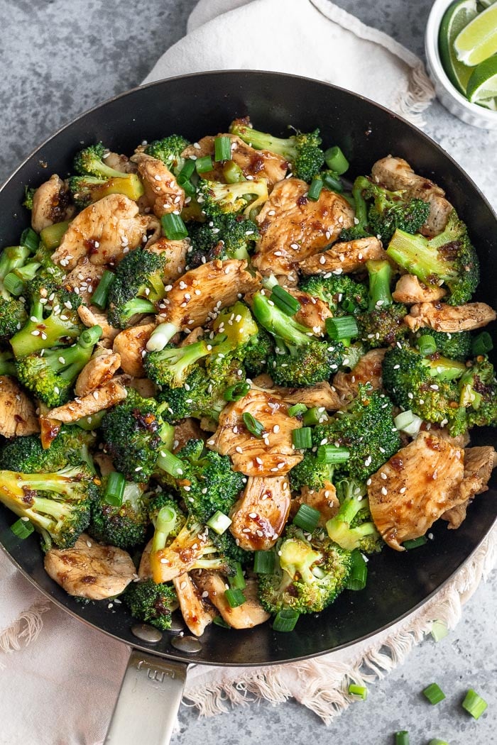 Overhead shot of Whole30 healthy chicken and broccoli in a pan garnished with green onions and sesame seeds.