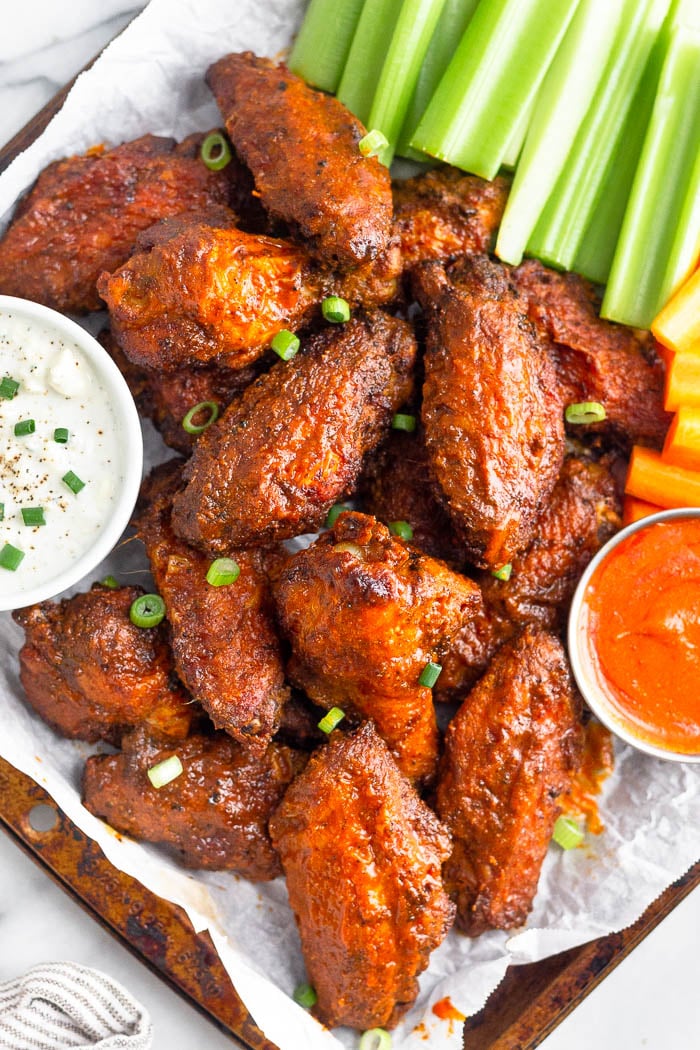 A tray of air fryer wings with blue cheese, hot sauce, celery, and carrots next to them.