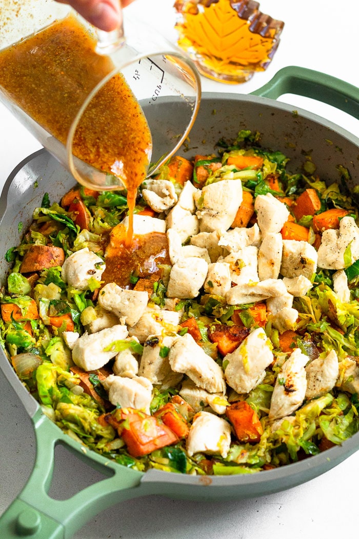 Skillet filled with sweet potatoes, shredded Brussel sprouts, and chicken with a maple mustard sauce being poured over top.