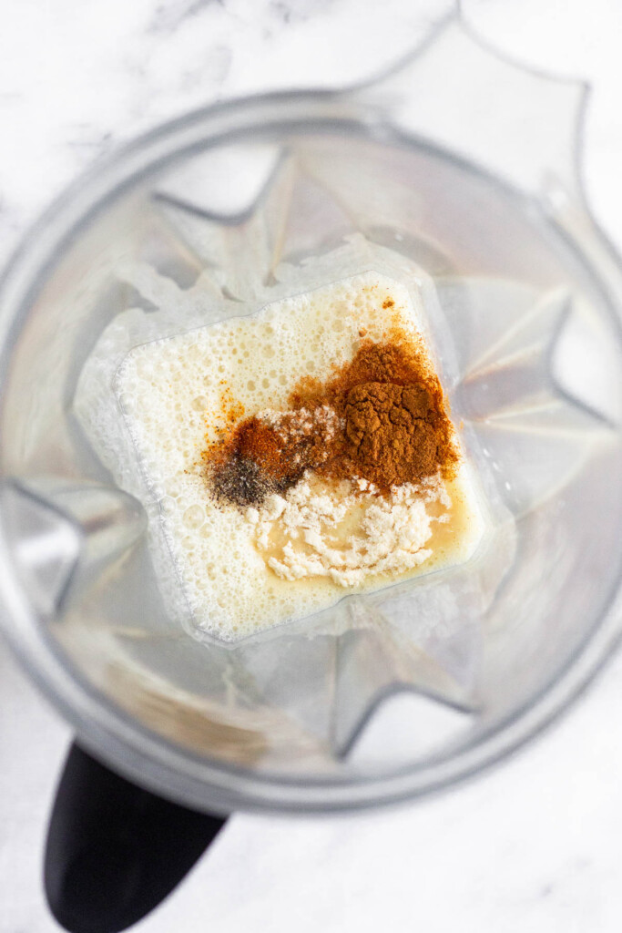 Blender filled with milk, a date, spices, collagen, ginger, and turmeric.