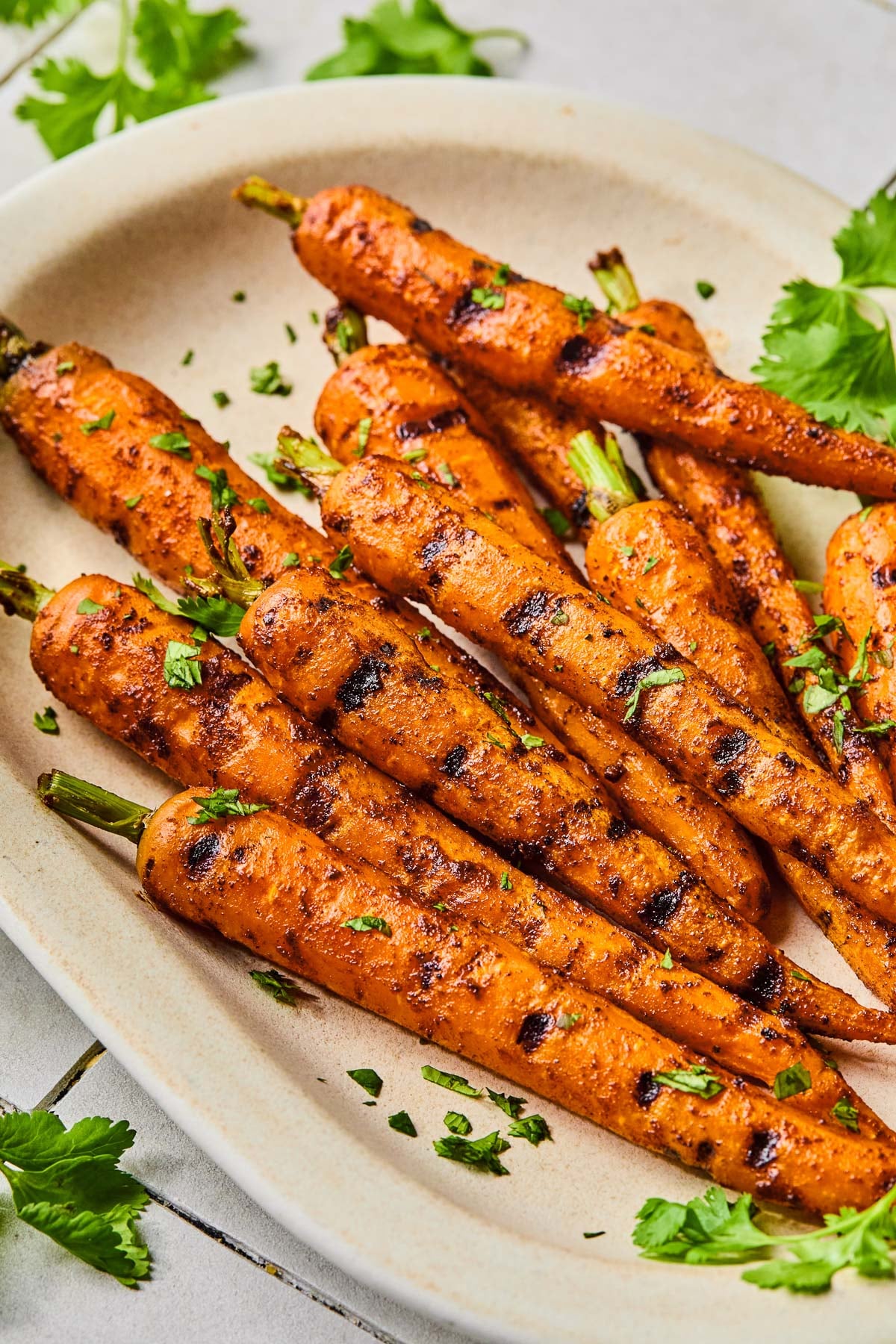 Grilled carrots on a serving platter topped with chopped cilantro. Around the platter is more fresh cilantro.