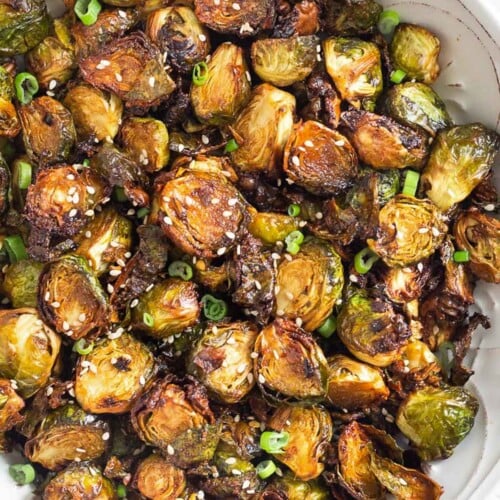 Large white bowl filled with crispy air fryer brussel sprouts garnished with sesame seeds and green onions.