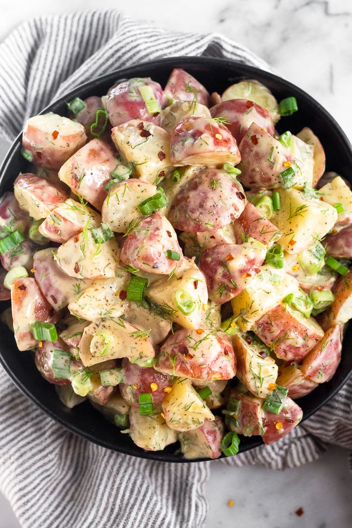 Honey mustard potato salad in a large bowl topped with green onions. The bowl is sitting on a striped kitchen towel.