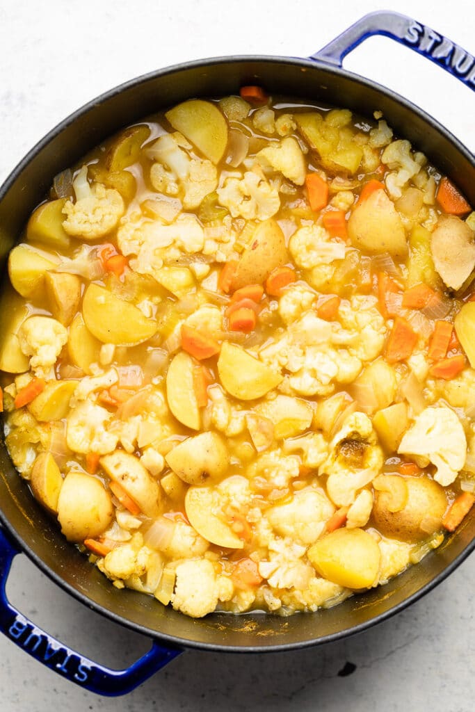 Large soup pot with cooked carrots, cauliflower, and potatoes in broth.