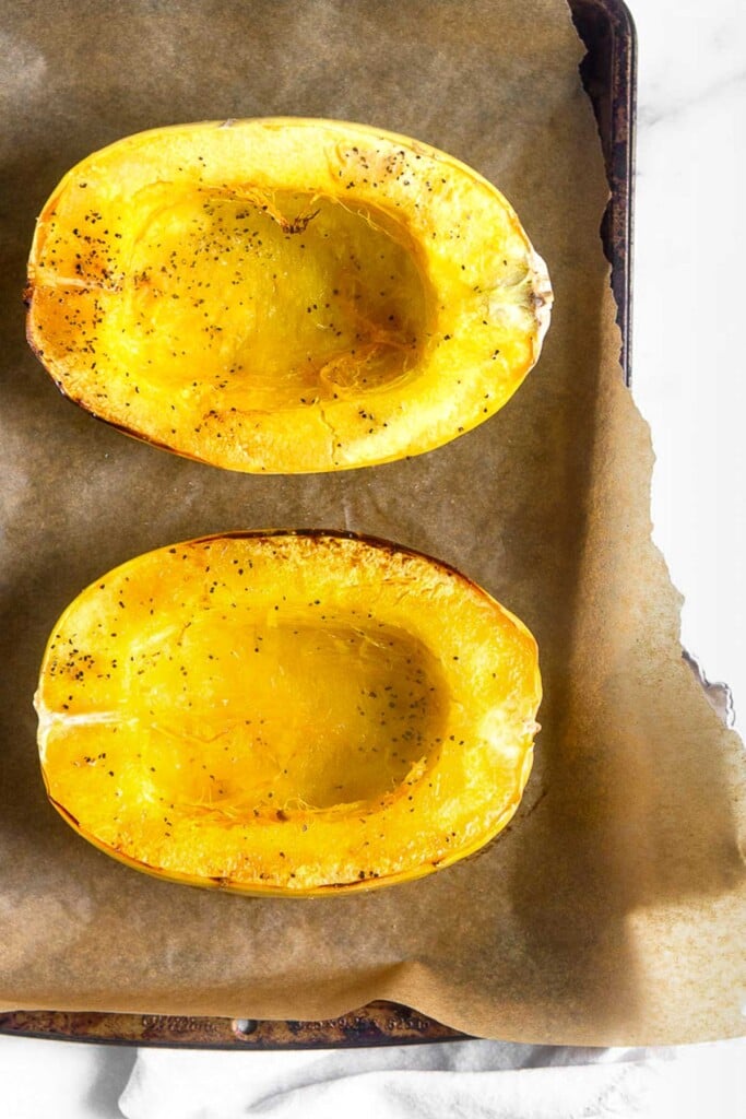 Baking sheet lined with parchment paper with two halves of spaghetti squash that have been baked.