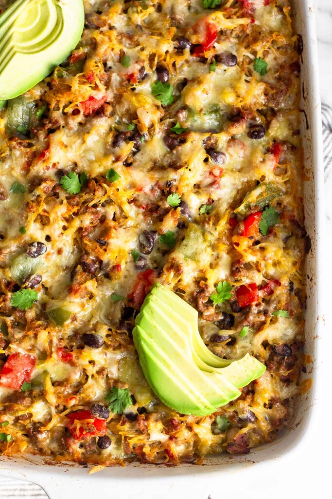 Overhead shot of baked spaghetti squash casserole topped with sliced avocado and cilantro in a white baking dish.