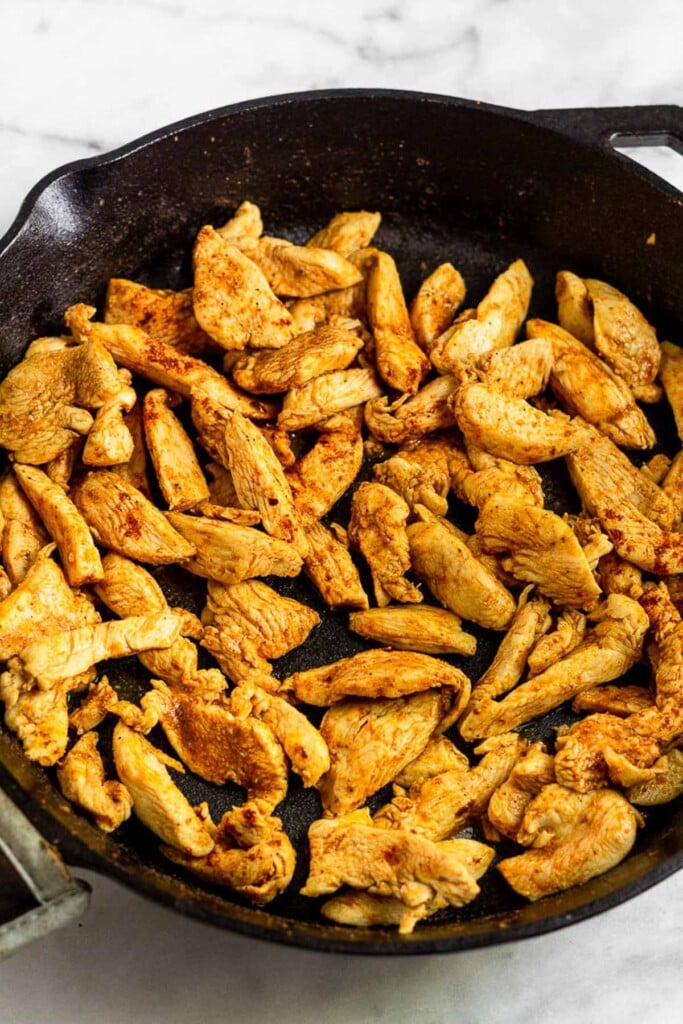 Large cast iron skillet filled with thinly sliced sautéed chicken.