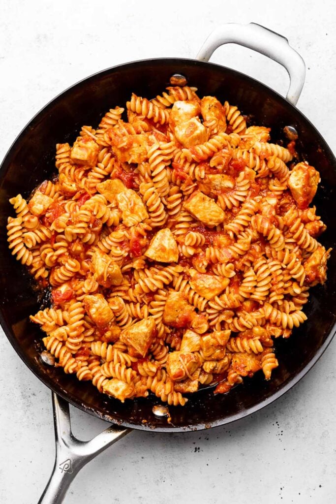 Skillet filled with cooked chicken, pasta, and pasta sauce all mixed together.
