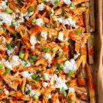 Sheet pan of buffalo chicken fries topped with blue cheese dressing, blue cheese crumbles, green onions, and fresh parsley.