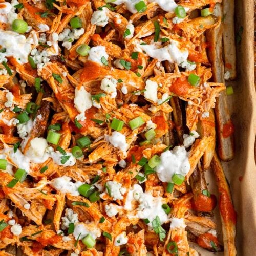 Sheet pan of buffalo chicken fries topped with blue cheese dressing, blue cheese crumbles, green onions, and fresh parsley.