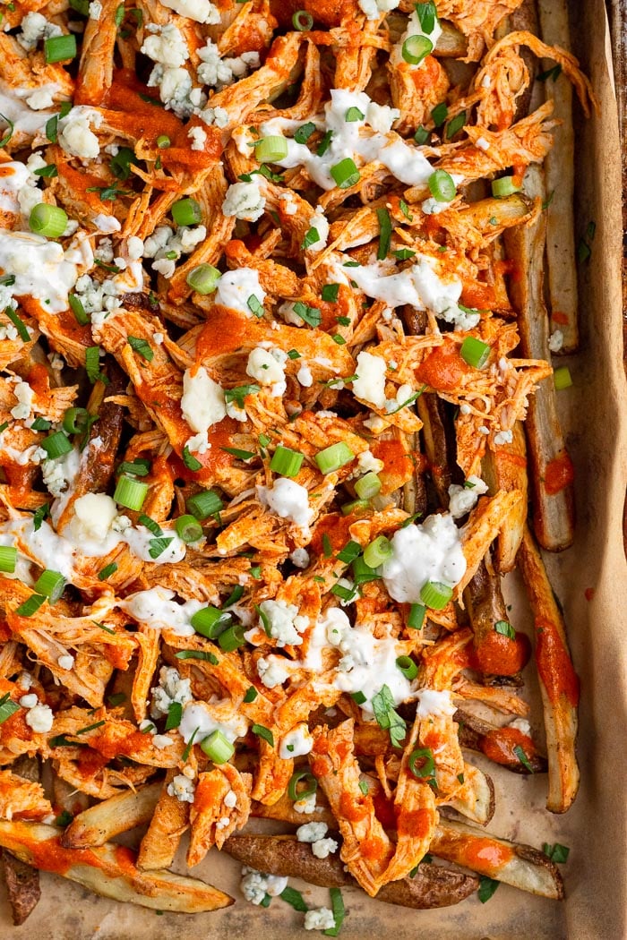 Sheet pan of buffalo chicken fries topped with blue cheese dressing, blue cheese crumbles, green onions, and fresh parsley.