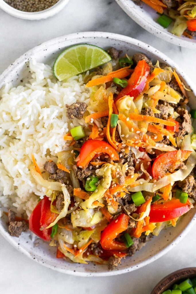 Close up of a plate of cabbage and beef stir fry, white rice, and a lime wedge.