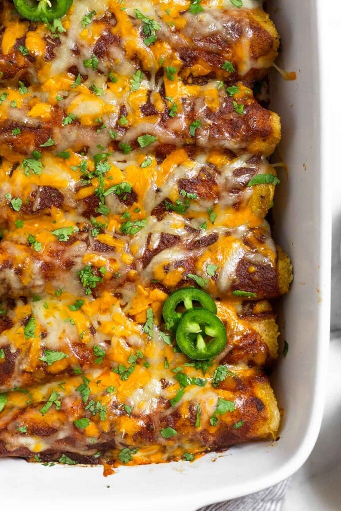 Chicken enchiladas with red sauce and cheese in a large dish garnished with cilantro and jalapeño slices.