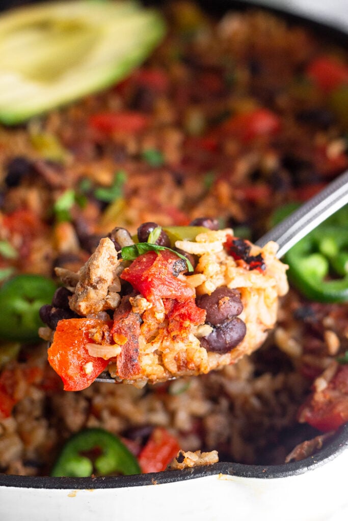 Spoon with a scoop of taco rice skillet in front of the whole dish in a cast iron.