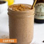 Coffee protein smoothie in a jar with some toppings on it and a straw in it. Around it is a jar of cold brew, coffee beans, and bananas.