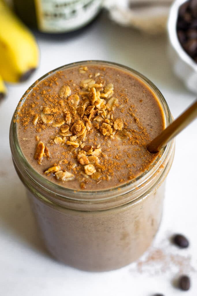 Overhead shot of a protein shake in a jar topped with granola and a straw in it.