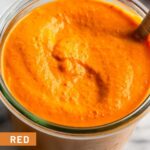 Jar filled with red pepper sauce with a spoon in it.