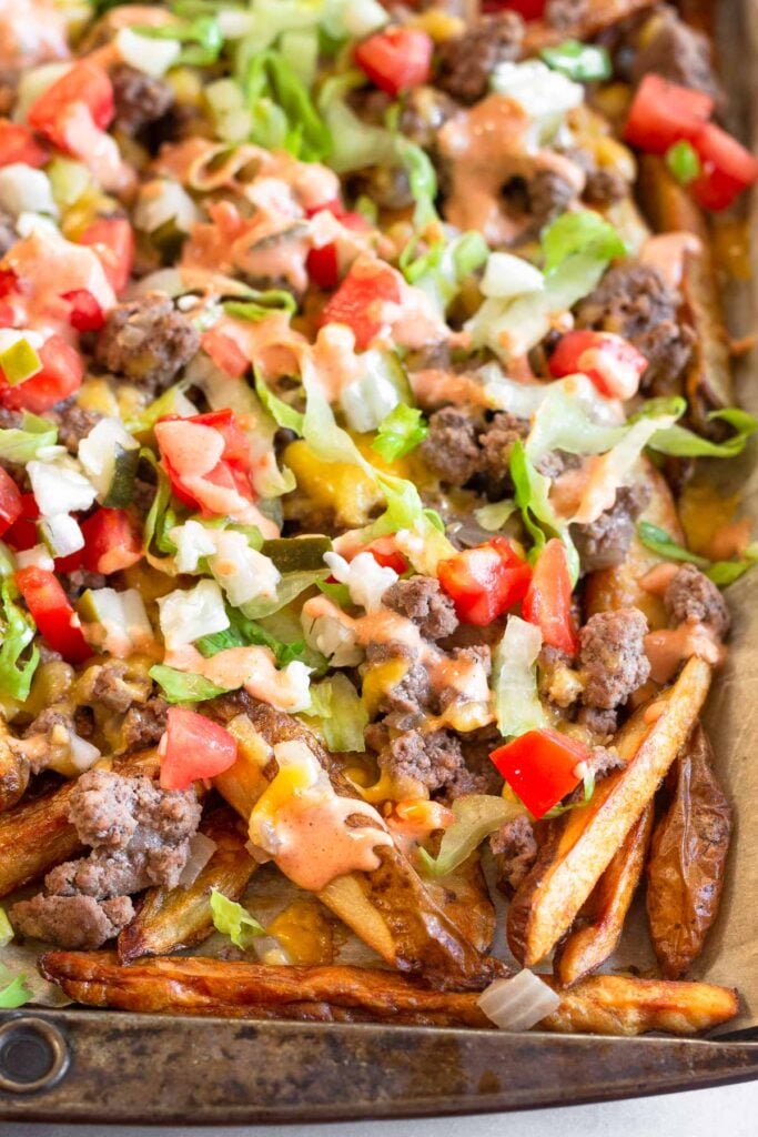 Cheeseburger fries on a large baking sheet topped with lettuce, tomato, pickles, and special sauce.